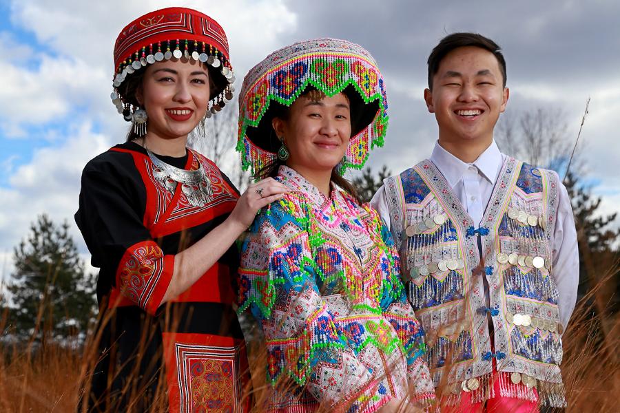 三名亚洲学生示范苗族传统服装、珠宝和故事布.