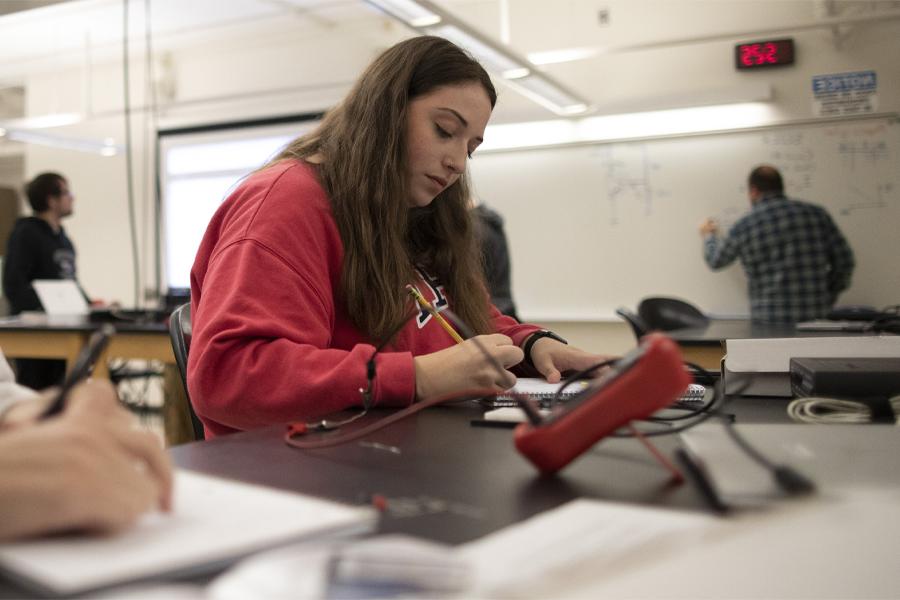 一个穿红衬衫的学生坐在工作桌旁，在记事本上做笔记.
