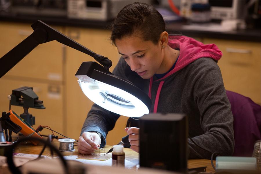 一名学生在一盏大灯下焊接一组组微型电线.