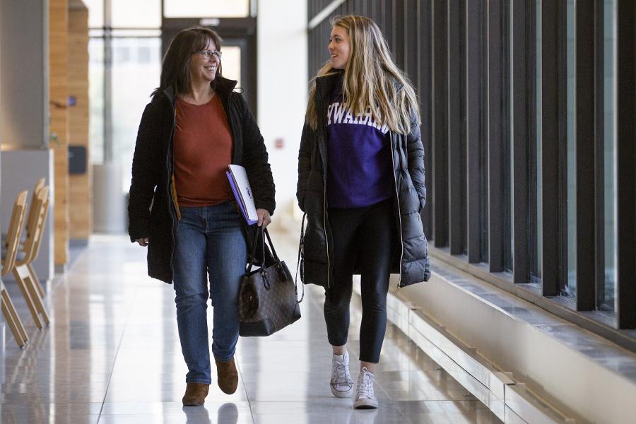一个学生和她的妈妈走在走廊上.