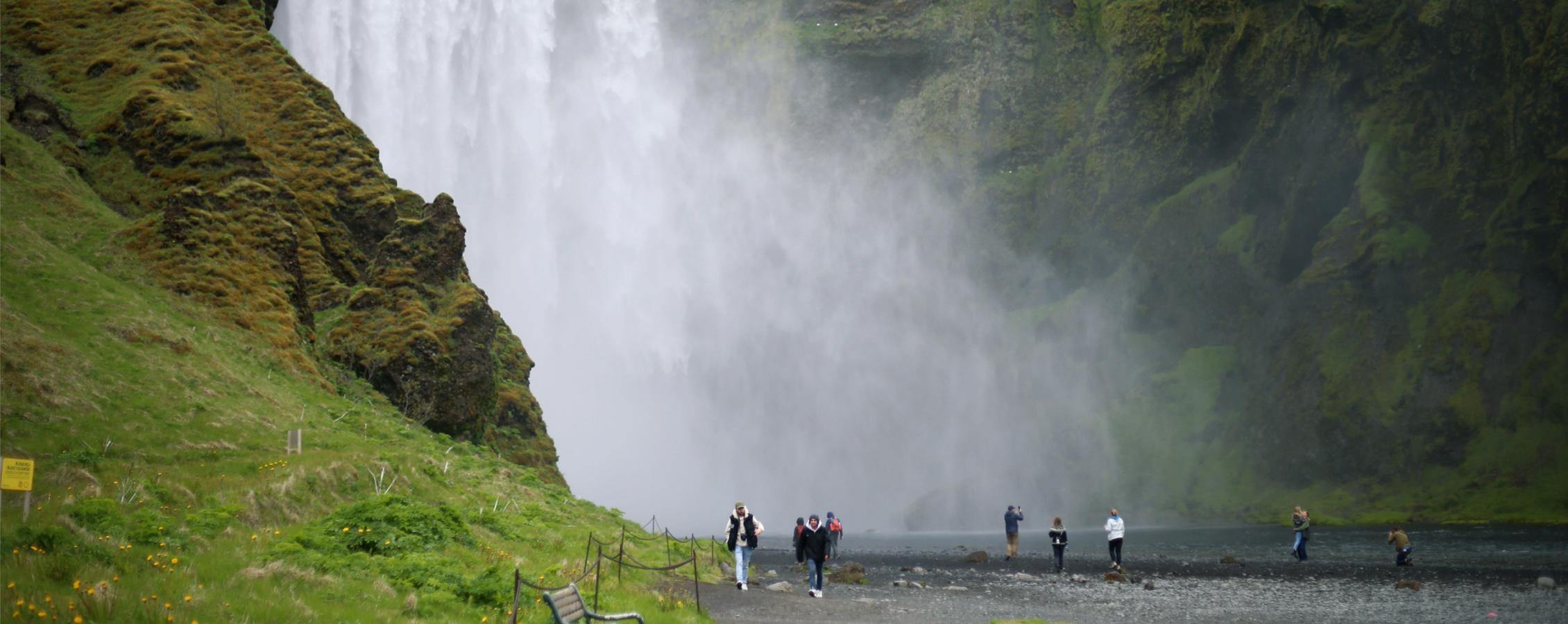 Students walk along a path by a waterfall.