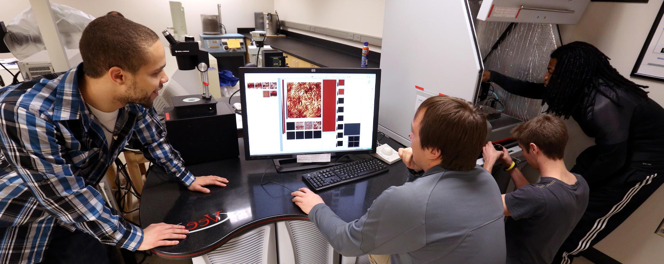 Students look at magnifications on a computer in the physics lab.