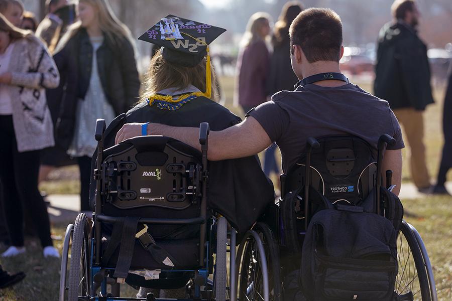 Two people in wheelchairs with their arms around each other.