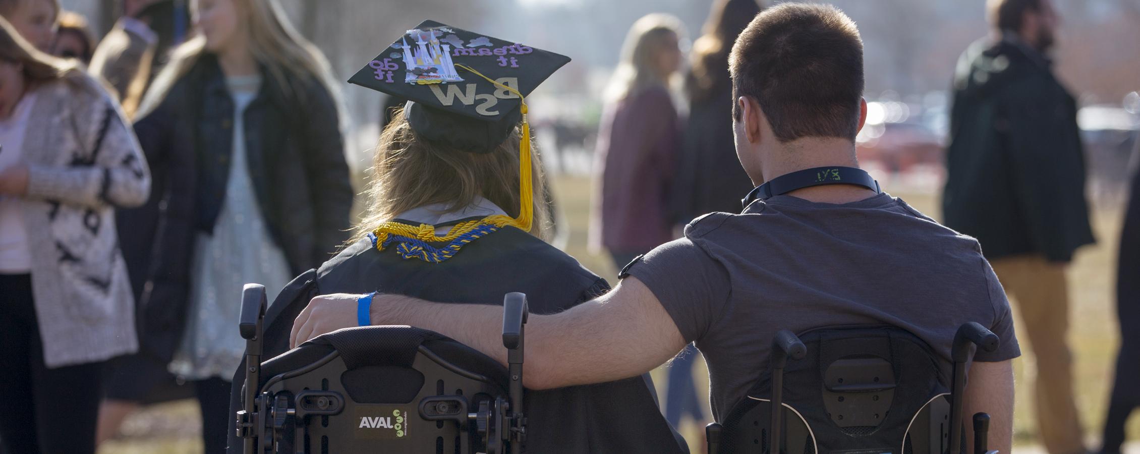 Two people in wheelchairs with their arms around each other at graduation.