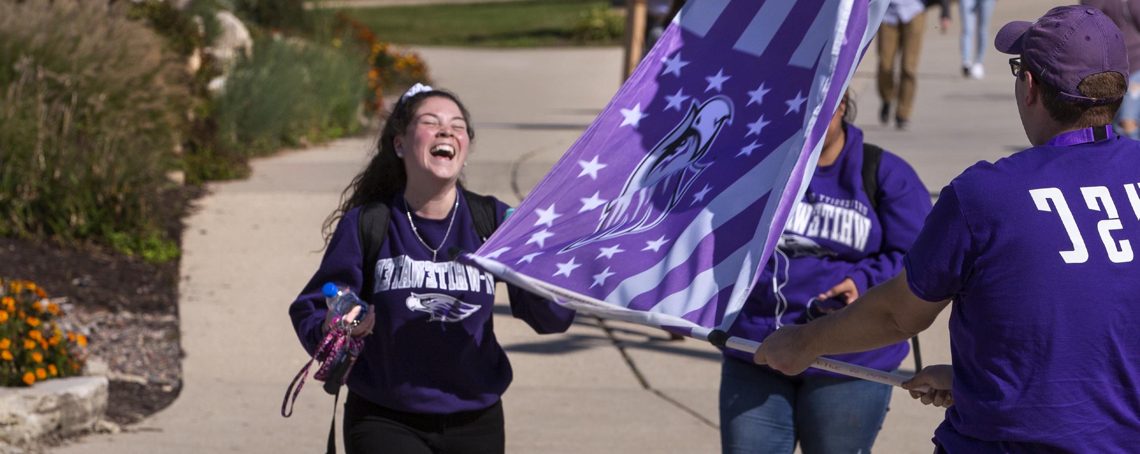 三个学生一起笑着，挥舞着紫色的战鹰旗.
