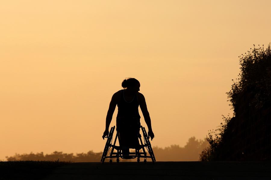 一个坐在轮椅上的人的剪影映衬着夕阳西下的天空.