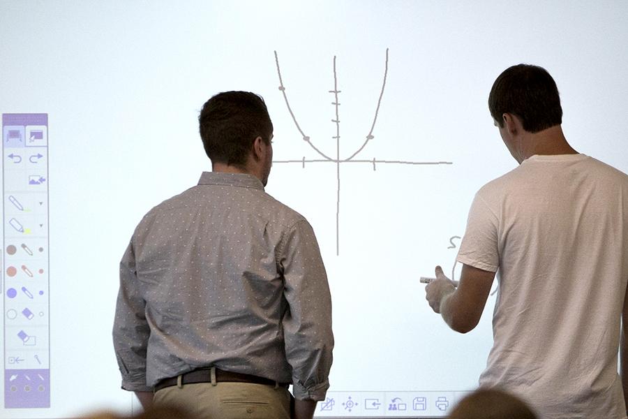 Two people at a white board drawing a graph.