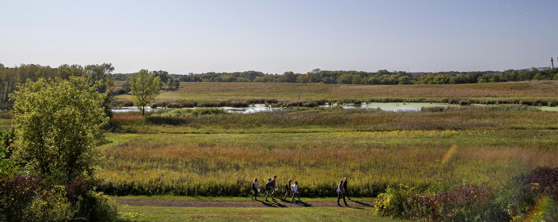 Students walk through an open field with a small body of water.