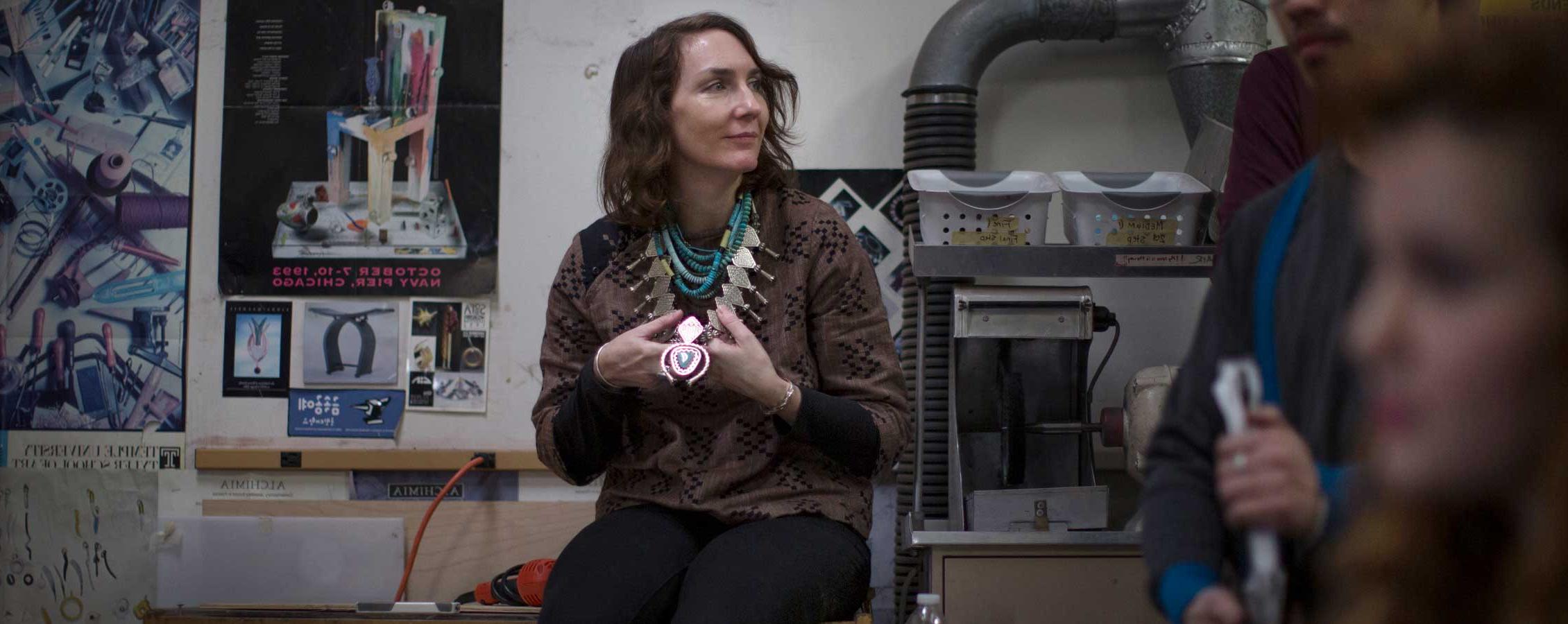 Teresa Faris sits on a table in a jewelry lab.