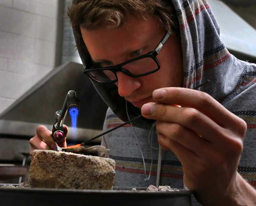 A student creates jewelry with a flame.