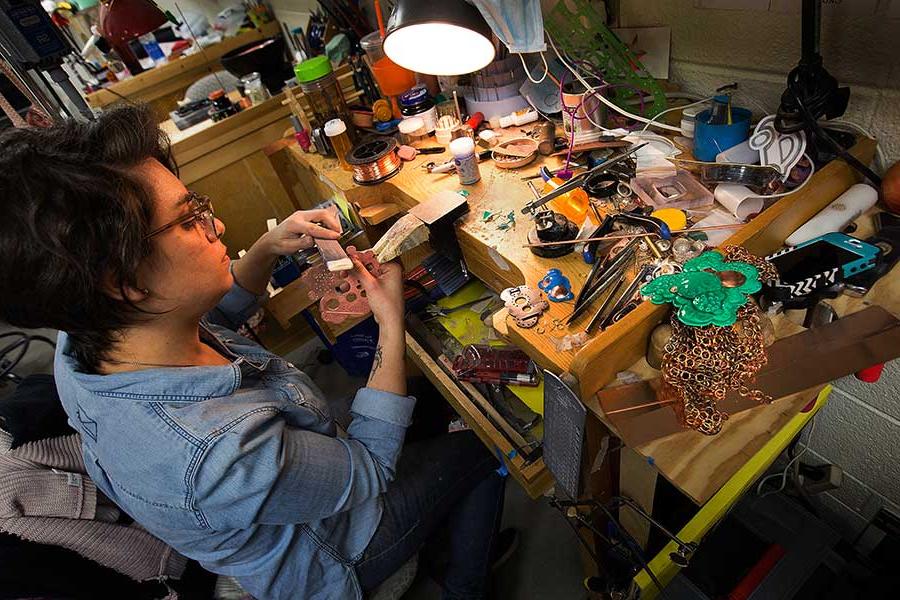 A student works at a wooden table covered in tools and materials.