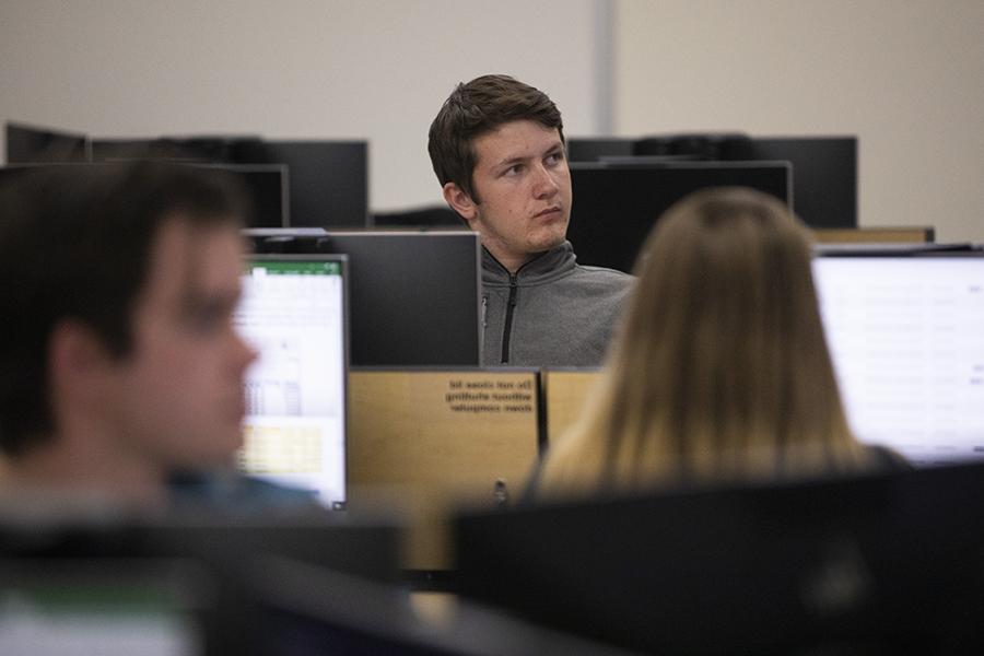 一个学生坐在电脑前，对着摄像头看向他的右边.