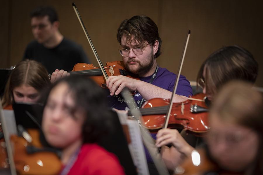 A student in a purple shirt plays a violin.